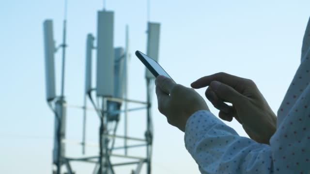 Men hand using phone with 5G telecommunications station tower background