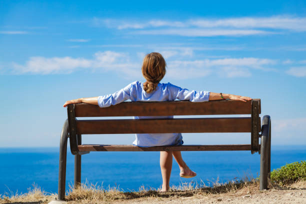 istock Woman sitting on a cliff bench above ocean / sea. 1225524210