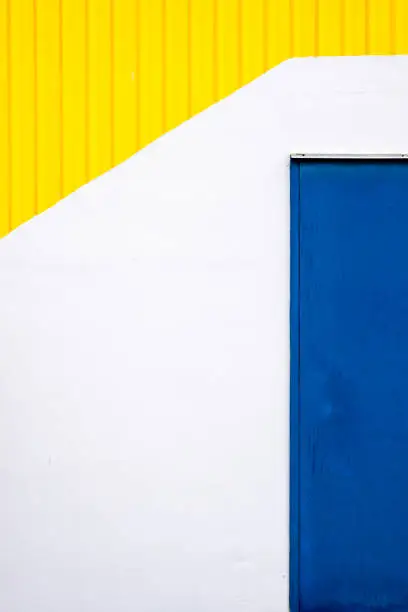 Blue close metalic door on a white and yellow wall. Minimal abstract photograph