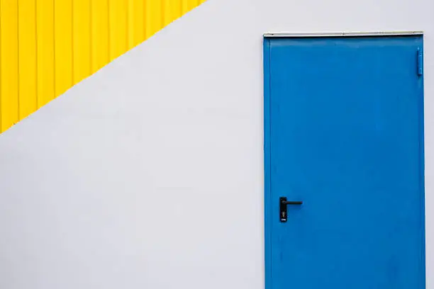 Blue close metalic door on a white and yellow wall. Minimal abstract photograph