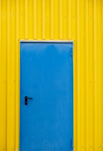 Blue close metalic door on a yellow wall. Minimal abstract photograph