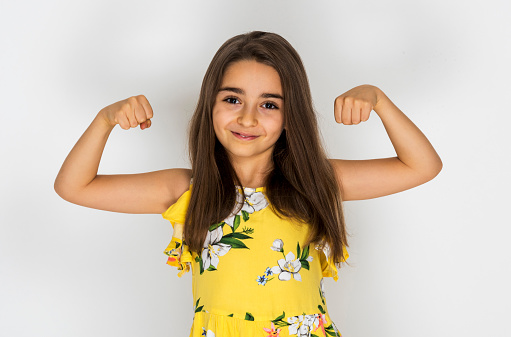 Funny happy little girl shows her muscles isolated on white background. Strength and power concept