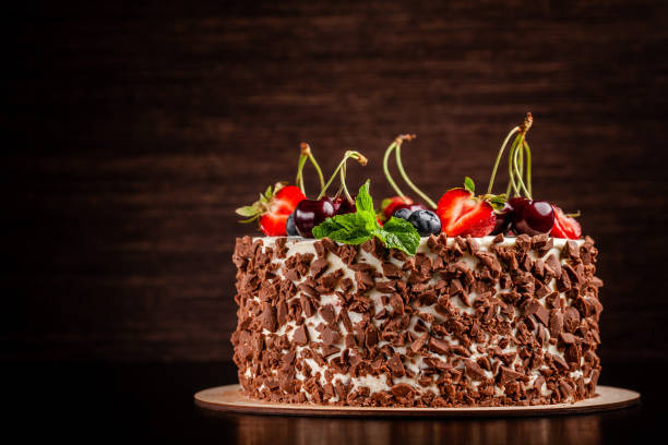 istock Chocolate sponge cake with white cream and berries, strawberries, cherries and mint. Cake cutaway on cinnamon background. copy space 1225530086