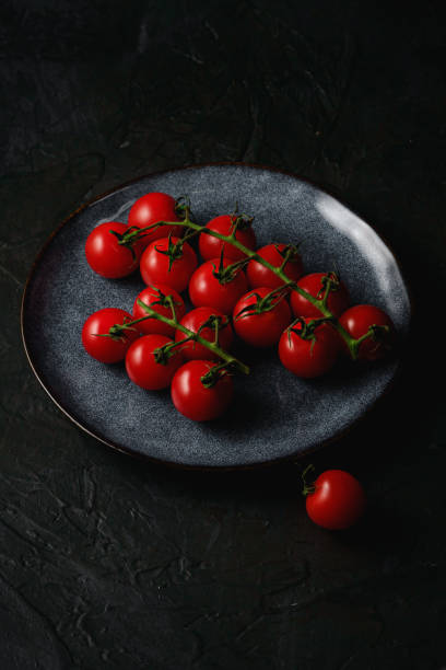 istock Cherry tomato branch, fresh ripe organic vegetables in grey plate on dark black textured background, angle view 1225530237