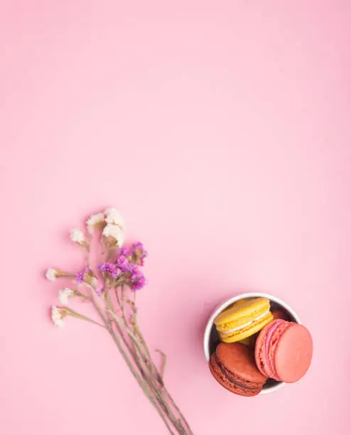 Photo of Colorful macarons in bowl  and flowers over on pink tender background. copy space, top view