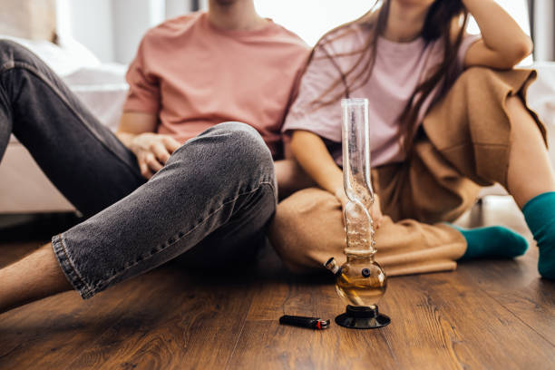 couple catch a buzz from using cannabis, marijuana caucasian couple catch a buzz from using cannabis, marijuana. man and woman enjoy using drugs together, they warm bong with cannabis and smoke it. drugs treatment, ganja and hemp medicine concept blunts stock pictures, royalty-free photos & images