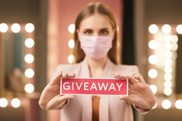 Photo of Woman Wearing Face Mask Holding Giveaway Sign