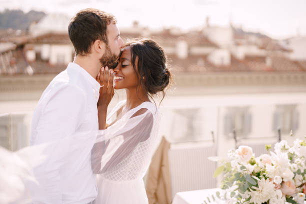 피렌체, 이탈리아에서 대상 파인 아트 결혼식입니다. 백인 신랑과 아프리카계 미국인 신부가 일몰 햇살 아래 옥상에서 껴안고 있습니다. 다인종 웨딩 커플 - couple sensuality embracing macho 뉴스 사진 이미지