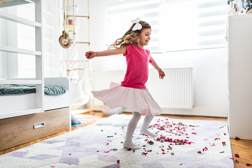 Photo of beautiful girl dancing in domestic room. Colorful confetti are on the floor. Celebration event during COVID-19 isolation.