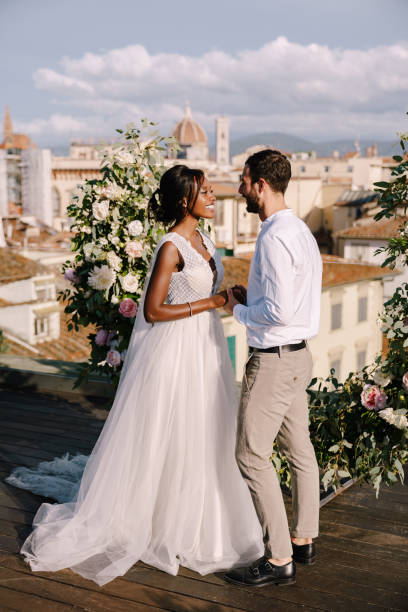 interracial hochzeitspaar. eine hochzeitszeremonie auf dem dach des gebäudes, mit blick auf das stadtbild auf die stadt und die kathedrale santa maria del fiore. reiseziel fine-art-hochzeit in florenz, italien - ringlet stock-fotos und bilder