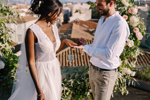 couples de mariage de race mixte - mariée afro-américaine et marié caucasien. le marié met une bague sur le doigt des mariées. destination mariage d’art à florence, italie. cérémonie de mariage sur le toit - young men young women bride hairstyle photos et images de collection