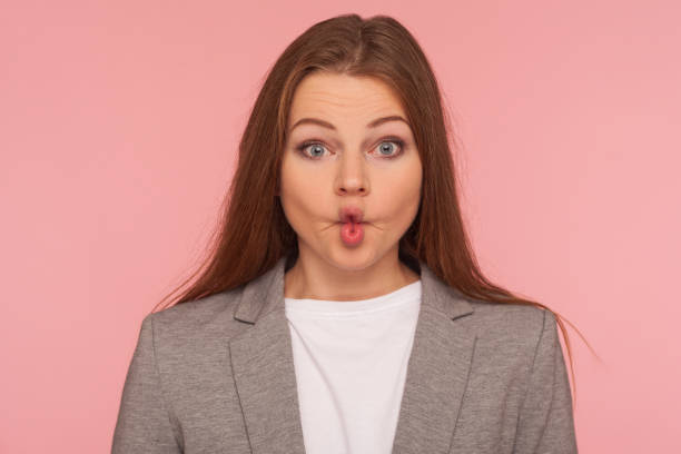 Closeup portrait of funny woman in business suit making fish face with pout lips, looking with humorous grimace Closeup portrait of funny pretty young woman in business suit making fish face with pout lips, looking with humorous goofy grimace, comical amazement. indoor studio shot isolated on pink background sucking lips stock pictures, royalty-free photos & images
