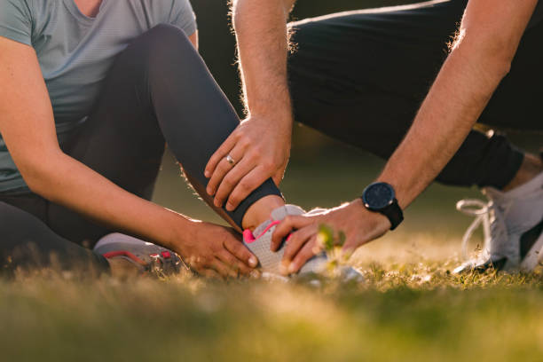 Let me help you with that injured ankle! Close up of unrecognizable man assisting his wife with ankle pain during sports training in nature. Copy space. athleticism stock pictures, royalty-free photos & images