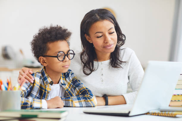 Mother and Son Using Laptop Portrait of cute African boy wearing big glasses while using laptop with mom, homeschooling and remote education concept one parent stock pictures, royalty-free photos & images