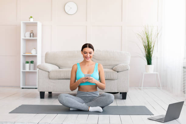 istock Fitness Girl Using Smartphone Watching Training Video On Laptop Indoors 1225550112