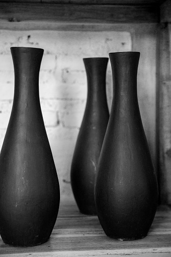 Three empty black ceramic vases on wooden shelf against concrete wall. Total black concept.
