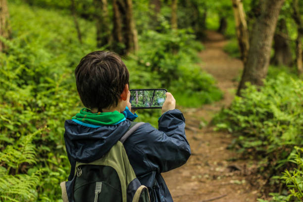 A child taking photos on a country footpath A young child boy casually dressed rucksack rain jacket holding and taking photos with a mobile device whilst on a footpath in a forest the background is blurred for copy space and the footpath journeys on into the distance ecosystem photos stock pictures, royalty-free photos & images