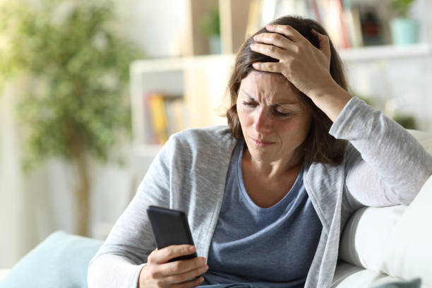sad adult woman reading news on phone at home - frustration emotional stress surprise women imagens e fotografias de stock