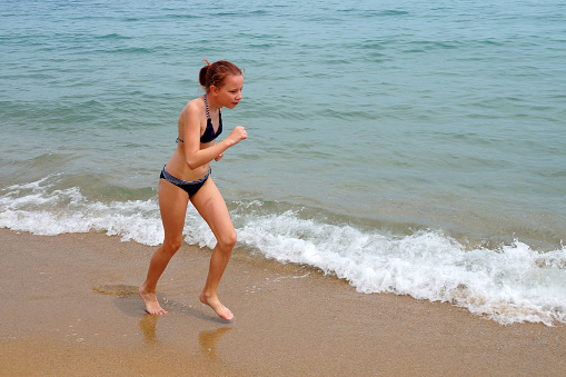 girl in a swimsuit runs along the sandy beach along the sea