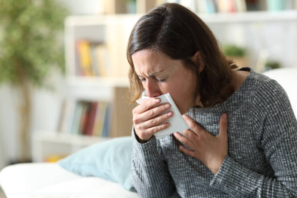 Sick adult woman coughing covering mouth with tissue at home Sick adult woman coughing covering mouth with tissue sitting on a couch at home nose flower stock pictures, royalty-free photos & images