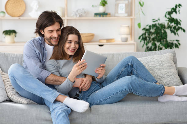 istock Cheerful couple cuddling on sofa at home, using digital tablet 1225552429
