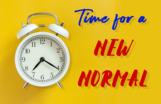 the new normal after COVID-19 Coronavirus pandemic concept. white alarm clock isolated on yellow background with text time for a new normal. a previously unfamiliar situation that has become standard
