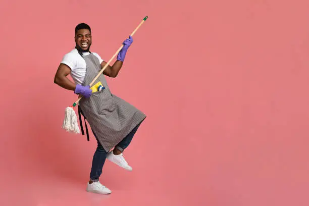 Photo of Funny African Man Using Mop Handle As Guitar, Having Fun During Cleaning