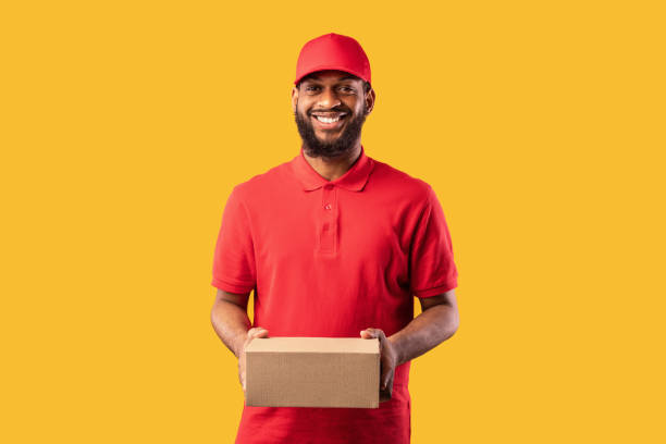 istock Black Courier Man In Uniform Holding Cardboard Box, Studio Shot 1225557595