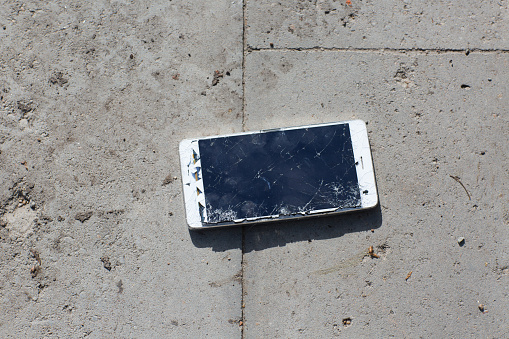 Broken screen mobile phone lies on ground.