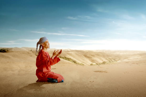 Asian Muslim man sitting while raised hands and praying with a blue sky background