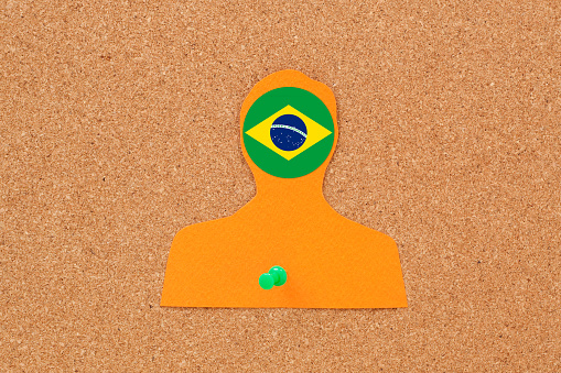 Paper silhouette of male pushpined to cork bulletin board with brazilian flag on his head