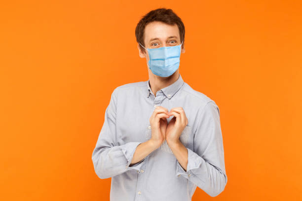 te amo. retrato de alegre joven trabajador con máscara médica quirúrgica de pie con gesto de amor del corazón y mirando a la cámara con sonrisa. - body care business healthcare and medicine looking at camera fotografías e imágenes de stock