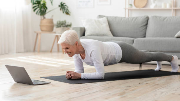 donna anziana sportiva che fa tavola yoga mentre guarda il tutorial su laptop - grandmother action senior adult grandparent foto e immagini stock