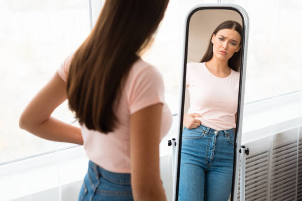 mulher triste medindo cintura após ganho de peso em pé em casa - preocupação com o corpo - fotografias e filmes do acervo