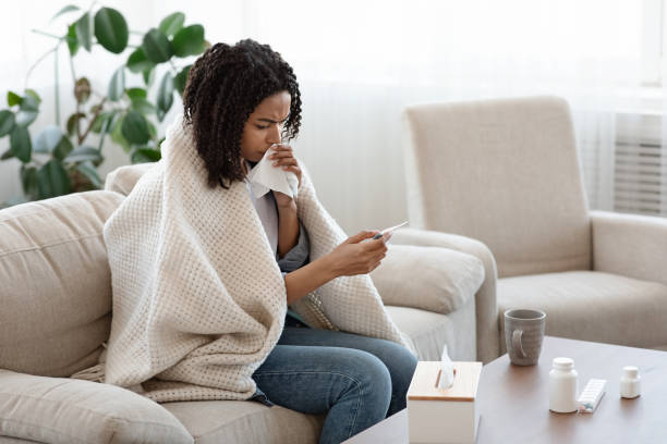 istock Sick african woman covered with blanket checking her temperature at home 1225571261