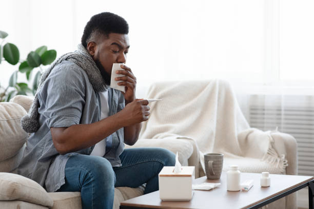 istock Covid-19 Symptoms. Ill Black Man Coughing And Checking Temperature At Home 1225571813