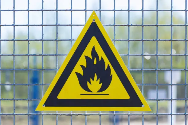 Photo of Black caution or warning fire triangle sign on yellow background or table on the painted grill of steel rods