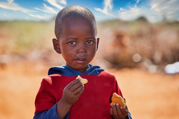 niño africano comiendo galletas en el patio - africa child village smiling fotografías e imágenes de stock