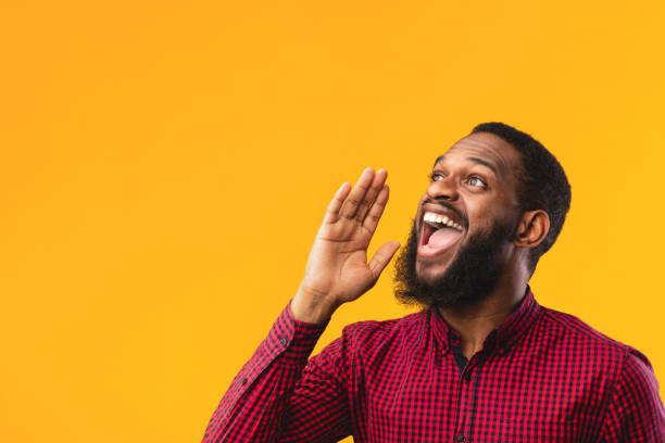 Black guy holding hand near mouth, screaming aside Making Announcement. Black guy holding hand near mouth, screaming aside at copy space over yellow background shouting stock pictures, royalty-free photos & images
