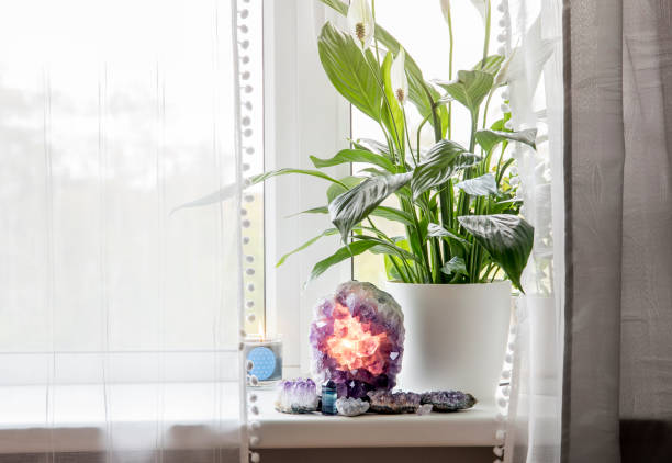 Using semi precious stone crystal details in home concept. Amethyst geode lamp burning, spiritual calming home atmosphere. Air cleaning plant flower Spathiphyllum, spath or peace lilie growing. Using semi precious stone crystal details in home concept. Amethyst geode lamp burning, spiritual calming home atmosphere. Air cleaning plant flower Spathiphyllum, spath or peace lilie growing. peace lily photos stock pictures, royalty-free photos & images