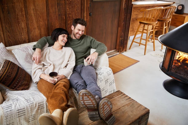 Couple talking and laughing while warming up with tea by their fireplace