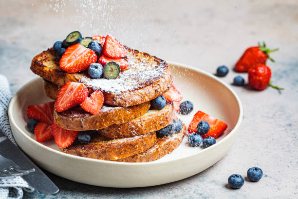Traditional French toasts with blueberries, strawberries and powdered sugar on white plate. Traditional French toast with blueberries, strawberries and powdered sugar on a white plate. sprinkling powdered sugar stock pictures, royalty-free photos & images