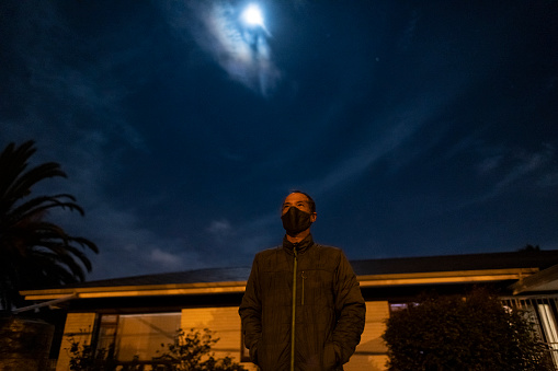 Man wearing protective mask outside home at night under full moon