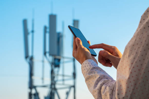 5g communications tower with man using mobile phone - tower imagens e fotografias de stock