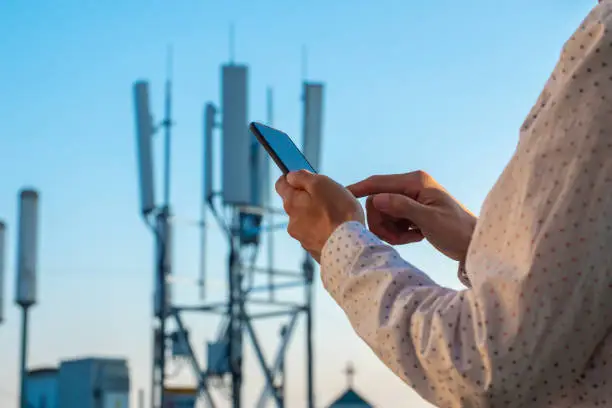 Men hand using phone with 5G Telecommunications base station tower background