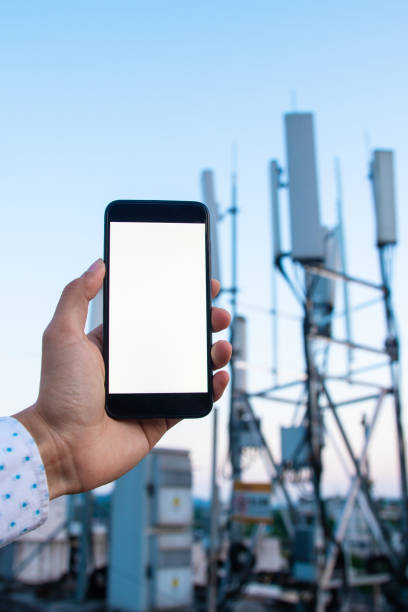 istock Man holding mobile phone with 5G communications tower background 1225586182