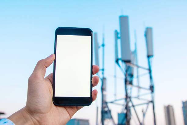 istock Man holding mobile phone with 5G communications tower background 1225586923