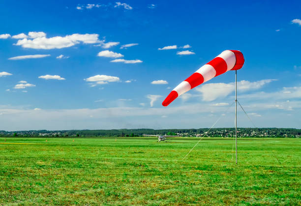 istock Red and white windsock wind sock on blue sky, green field and clouds background on aerodrome or airdrome. Shows wind speed and direction. 1225587858