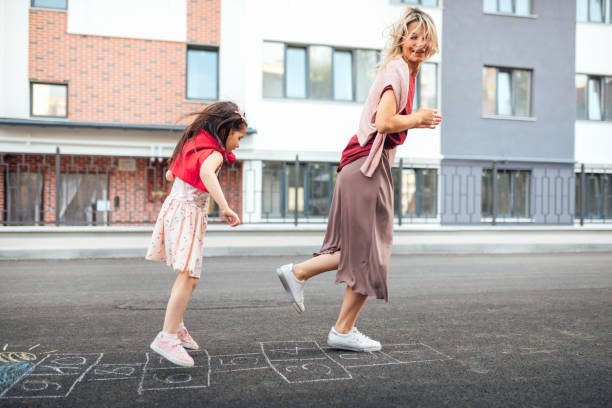 야외 놀이터에서 그녀의 어머니와 함께 홉스코치를 연주하는 행복한 어린 소녀의 야외 이미지. 아이는 밖에서 그녀의 엄마와 함께 놀고 있다. 아이는 포장도로에 그려진 홉스코치를 연기한다. � - little girls sidewalk child chalk 뉴스 사진 이미지