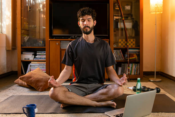 istock Man in the lotus position, performing yoga practice through online video classes 1225591457